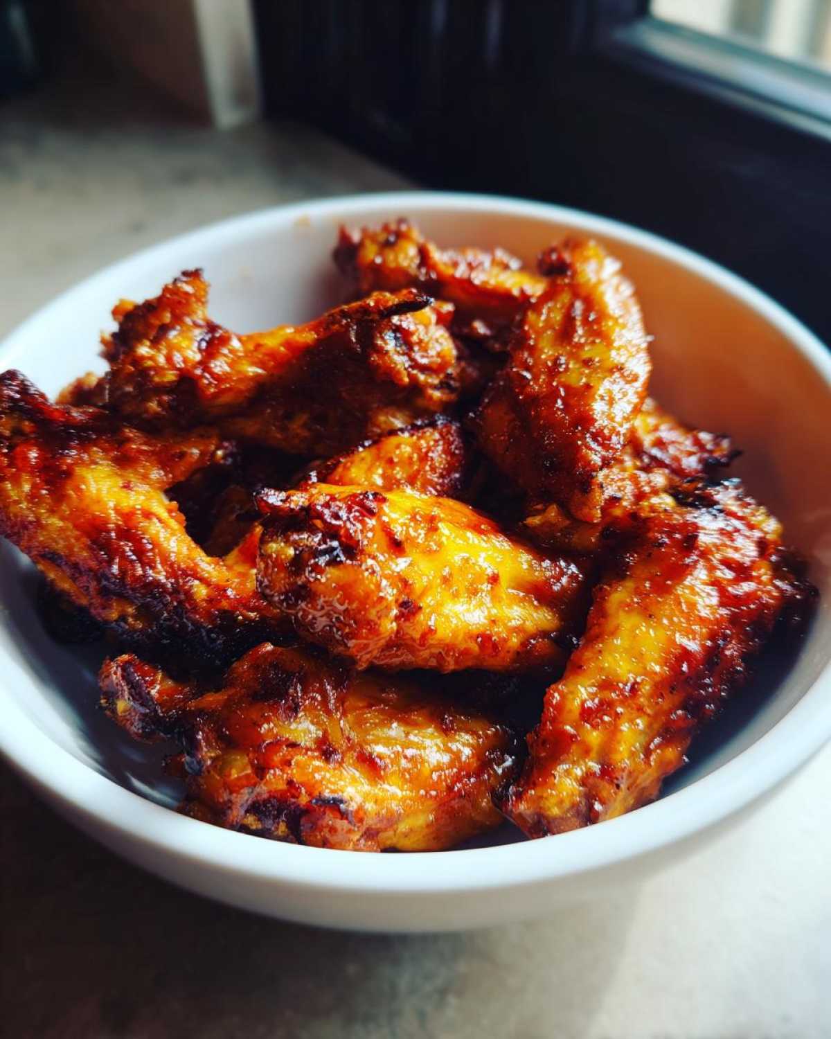 Close-up of crispy, saucy buffalo wings piled high in a small white bowl.