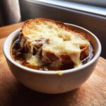 A close-up of a bowl of rich crockpot french onion soup topped with a toasted crouton covered in melted, gooey cheese.