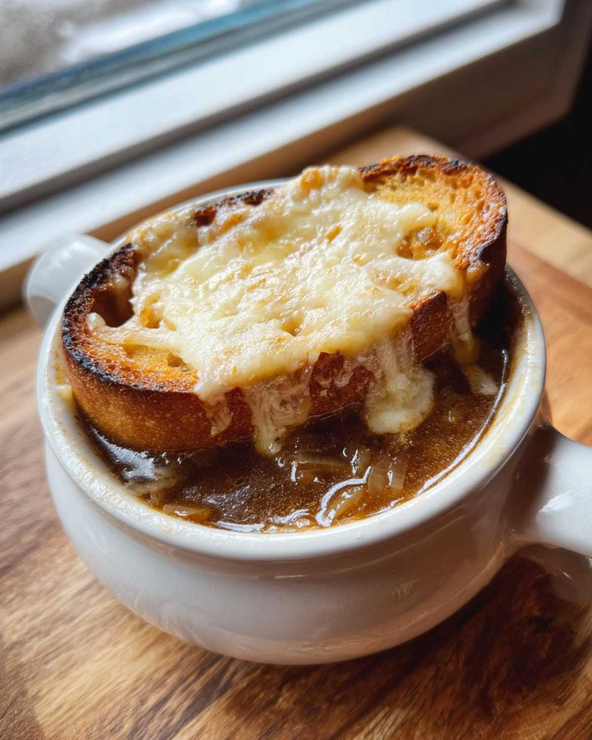 A close-up of rich crockpot french onion soup topped with melted cheese over toasted bread in a white crock.