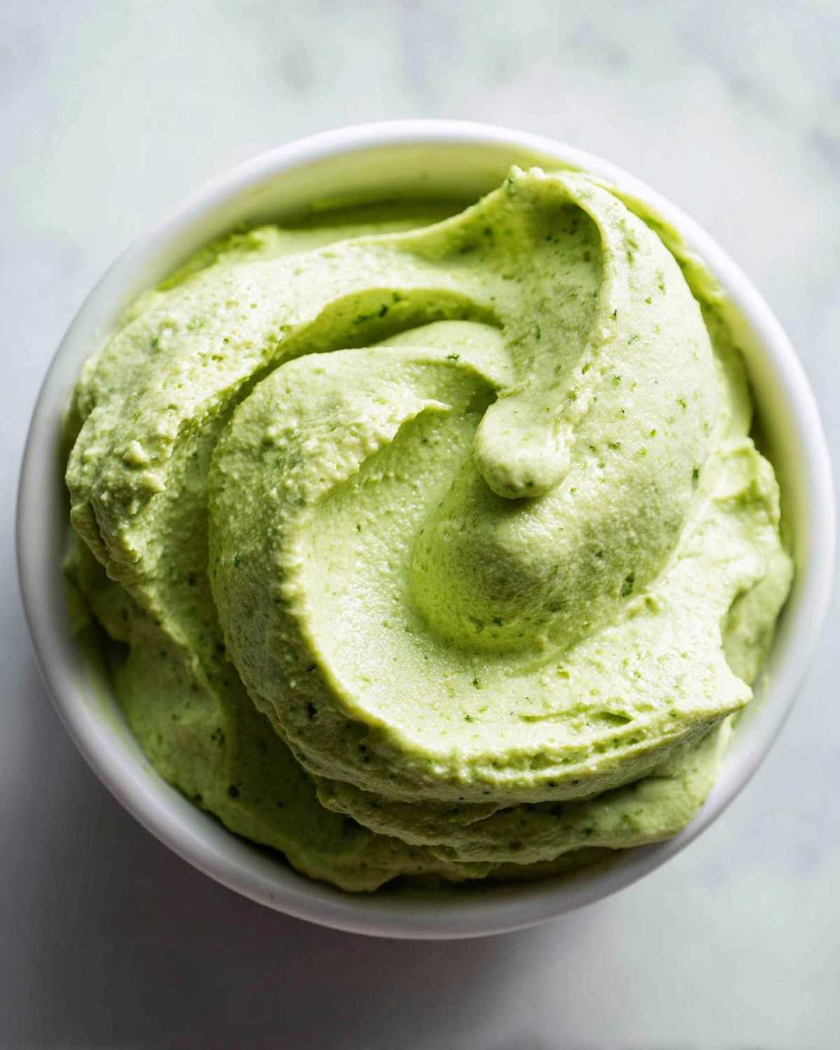 Overhead shot of thick, vibrant green Easy 5-Minute Salsa Verde Yogurt Dip swirled in a white bowl.