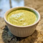 Close-up of a small white ramekin filled with creamy, light green Easy 5-Minute Salsa Verde Yogurt Dip.