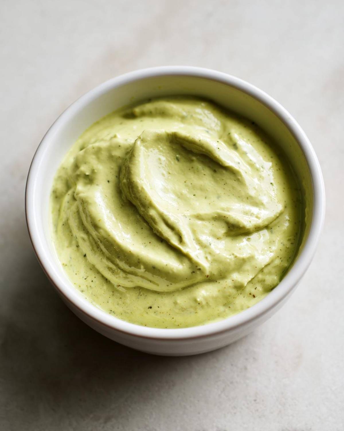 Close-up of thick, light green Easy 5-Minute Salsa Verde Yogurt Dip swirled in a small white bowl.
