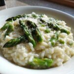Close-up of a bowl of Easy Creamy Asparagus Risotto topped with bright green asparagus spears and grated Parmesan cheese.