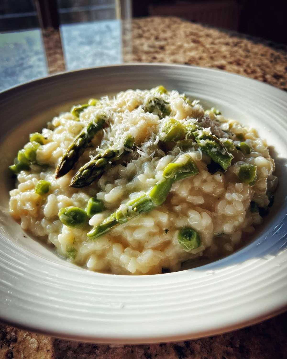 A close-up of a bowl filled with Easy Creamy Asparagus Risotto, topped with grated Parmesan cheese and bright green asparagus pieces.