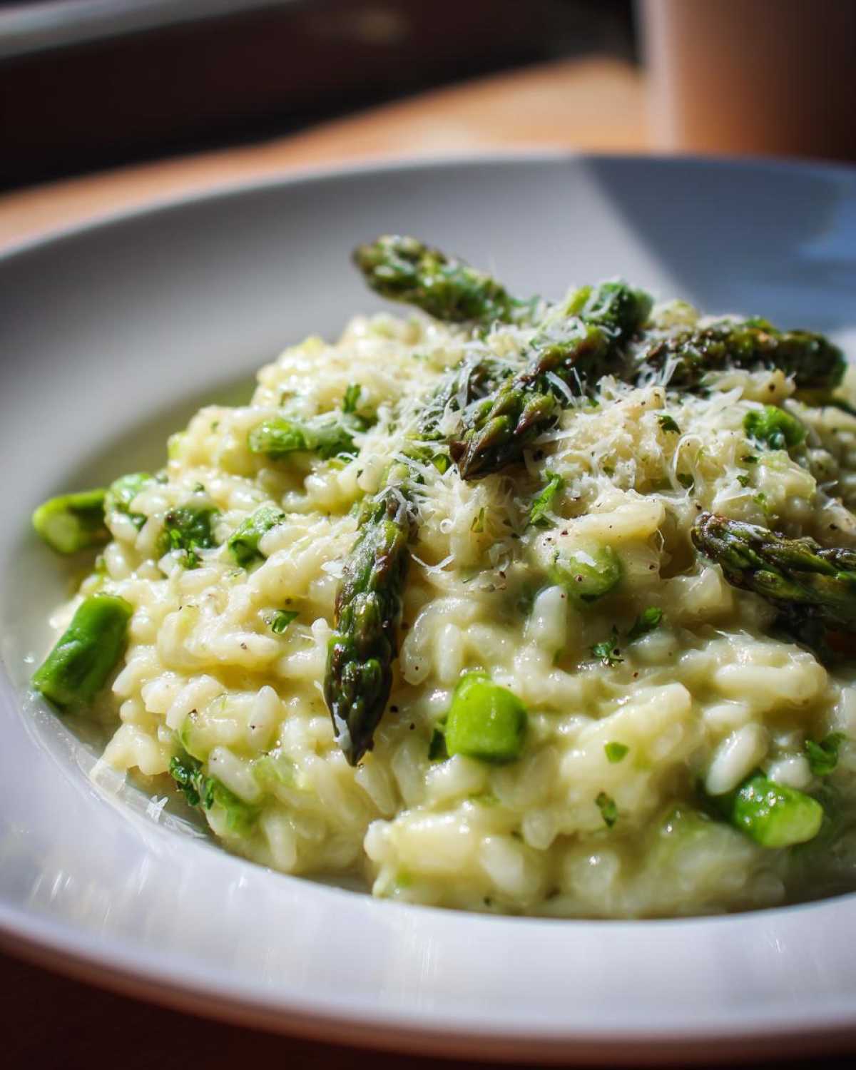 Close-up of a bowl of Easy Creamy Asparagus Risotto topped with whole asparagus spears and grated Parmesan cheese.