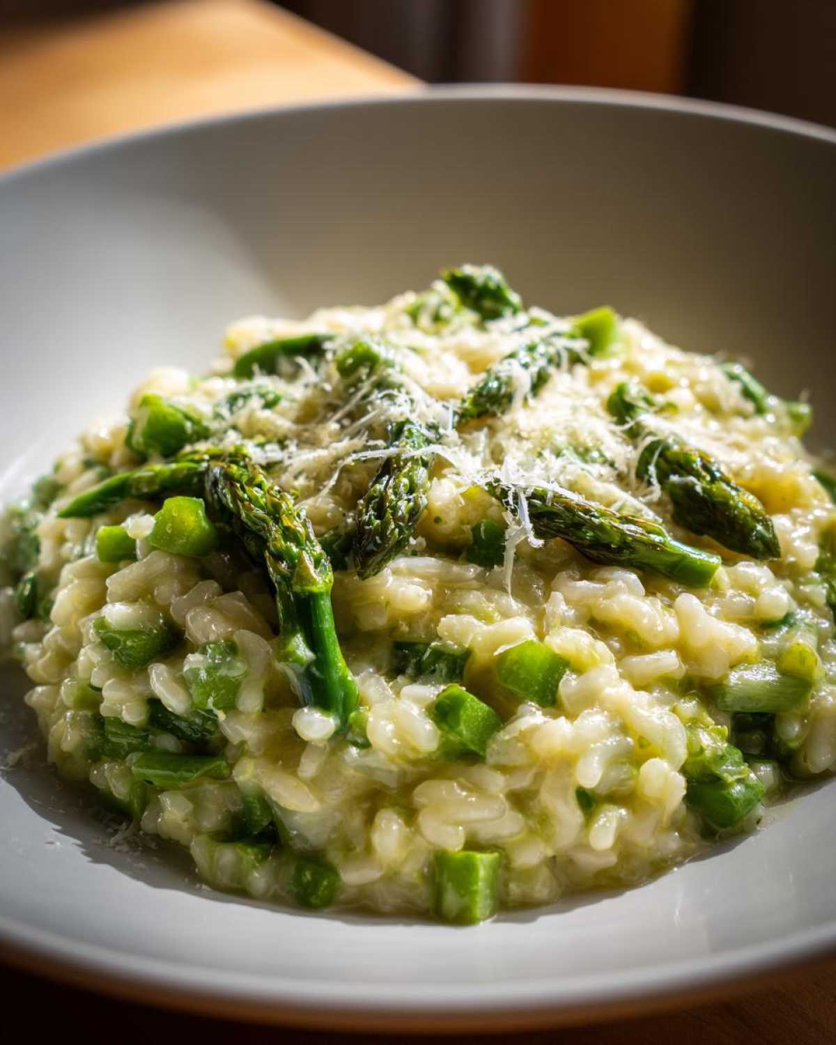 A close-up of a bowl of Easy Creamy Asparagus Risotto topped with grated Parmesan cheese and whole asparagus tips.