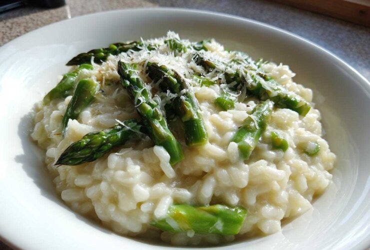 Close-up of a bowl of Easy Creamy Asparagus Risotto topped with bright green asparagus spears and grated Parmesan cheese.
