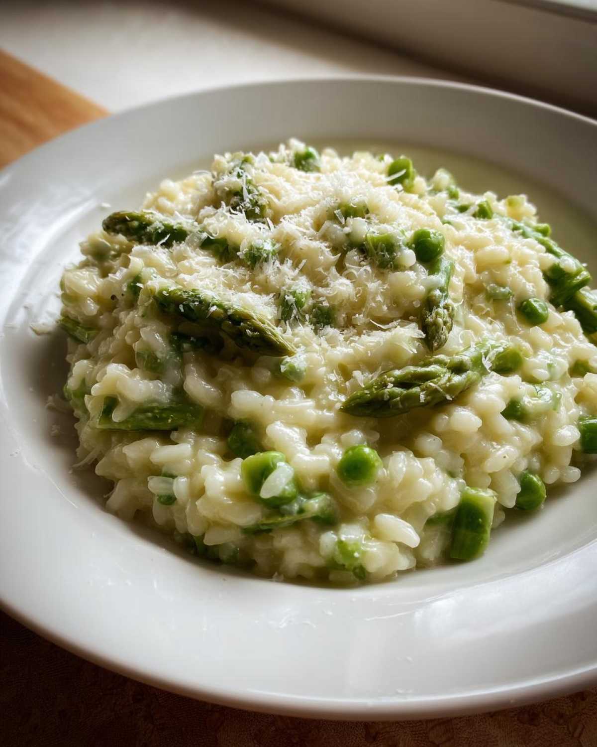 A close-up of creamy Easy Creamy Asparagus Risotto topped with grated Parmesan cheese and green peas.