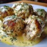 Close-up of Easy Creamy Greek Chicken Meatballs covered in a creamy dill sauce, one meatball is broken open.