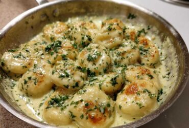 Close-up of Easy One-Pan Creamy Garlic Butter Gnocchi simmering in a stainless steel skillet, topped with fresh parsley.