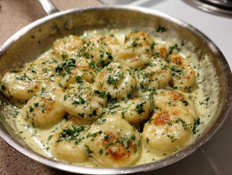Close-up of Easy One-Pan Creamy Garlic Butter Gnocchi simmering in a stainless steel skillet, topped with fresh parsley.