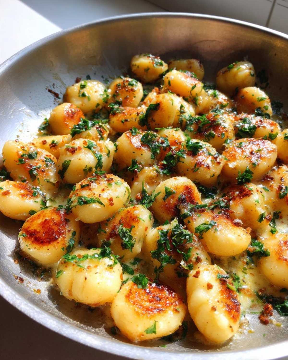 Close-up of golden-brown, pan-seared gnocchi tossed in a creamy garlic butter sauce and topped with fresh parsley, ready to eat.