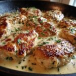 Close-up of seared chicken cutlets simmering in a creamy garlic lemon sauce, garnished with parsley.