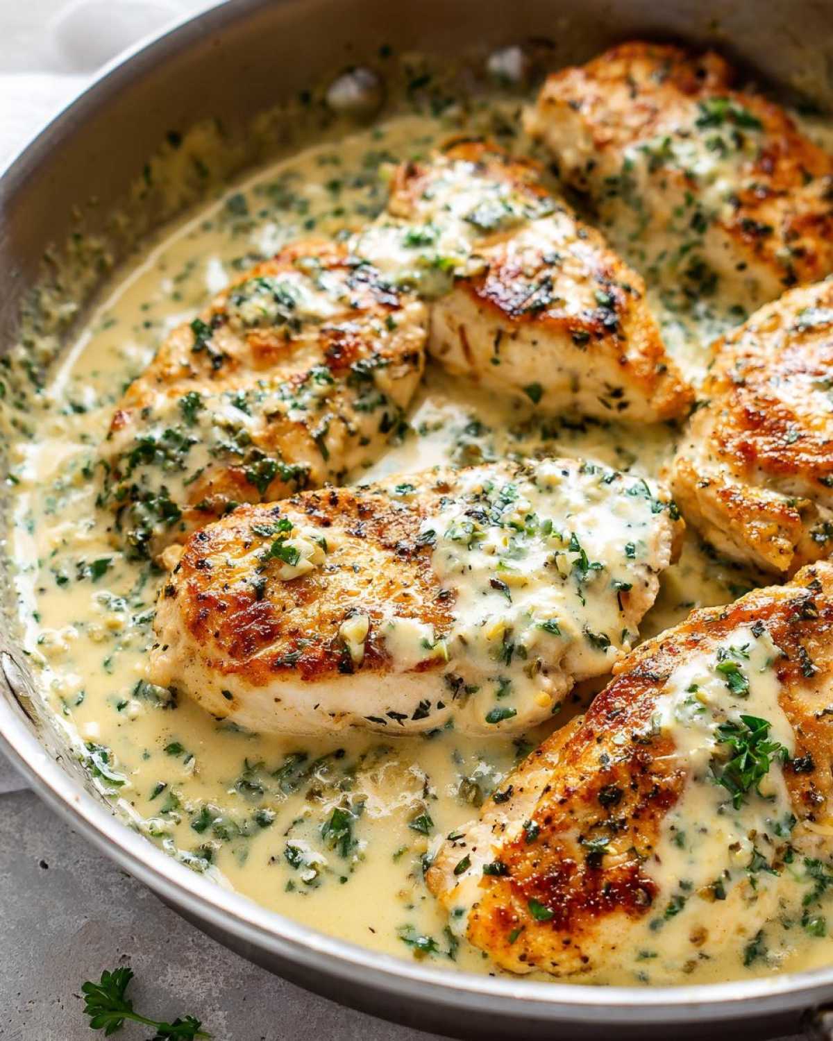 Close-up of seared chicken cutlets simmering in a creamy garlic lemon sauce with fresh parsley.