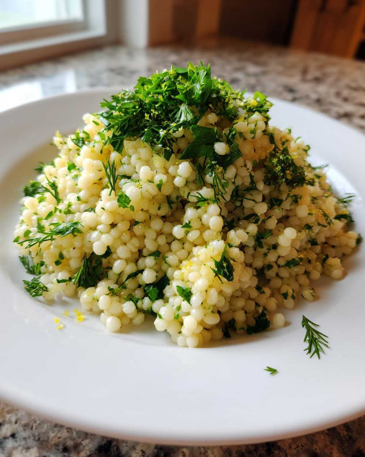 A close-up serving of Easy One-Pot Creamy Lemon Herb Couscous topped generously with fresh chopped parsley and lemon zest.
