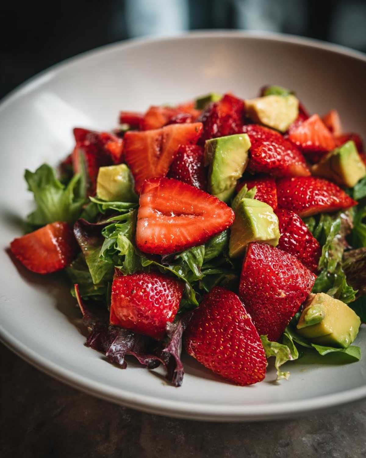 Close-up of a fresh Easy Strawberry Avocado Salad featuring bright red strawberries and green avocado chunks over mixed greens.