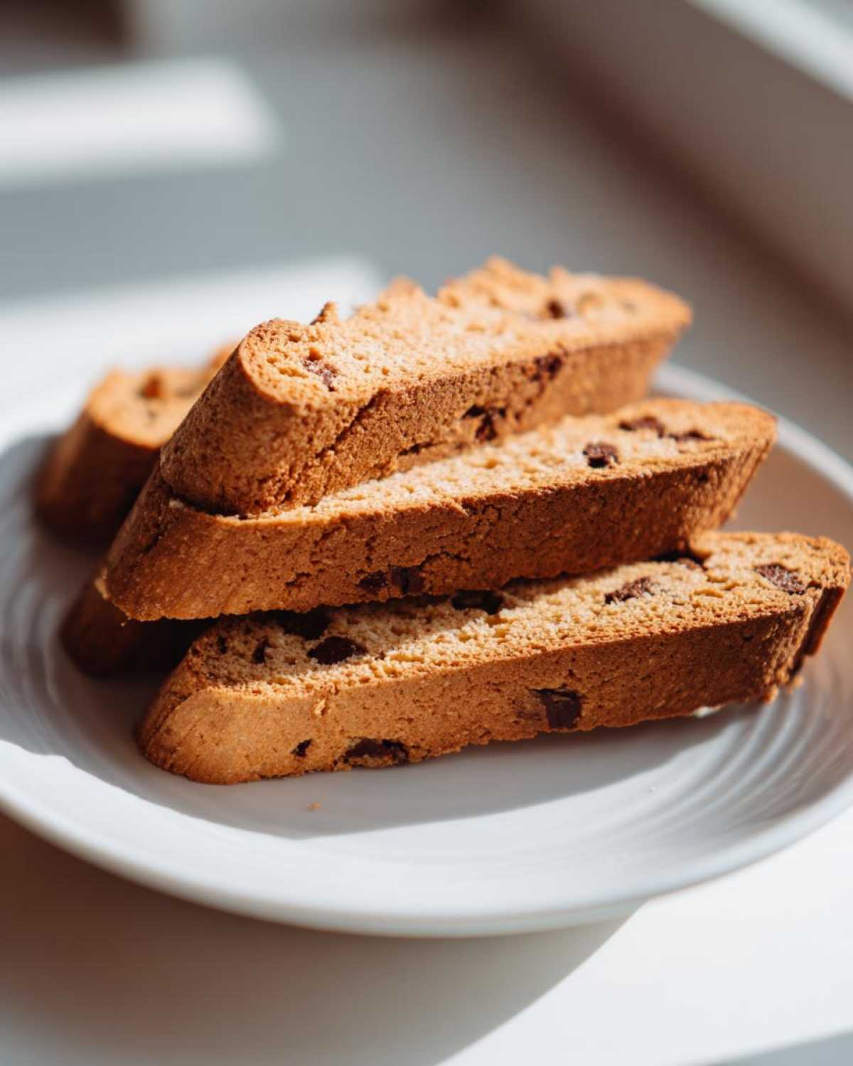 Close-up of three stacked slices of golden brown Gluten-Free Chocolate Chip Biscotti on a white plate.