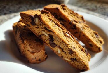 Close-up of three slices of golden brown Gluten-Free Chocolate Chip Biscotti, studded with chocolate chips and almonds, resting on a white plate.