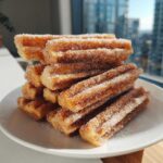 A stack of crispy Gluten-Free Cinnamon Sugar Waffle Sticks heavily coated in sparkling cinnamon sugar on a white plate.