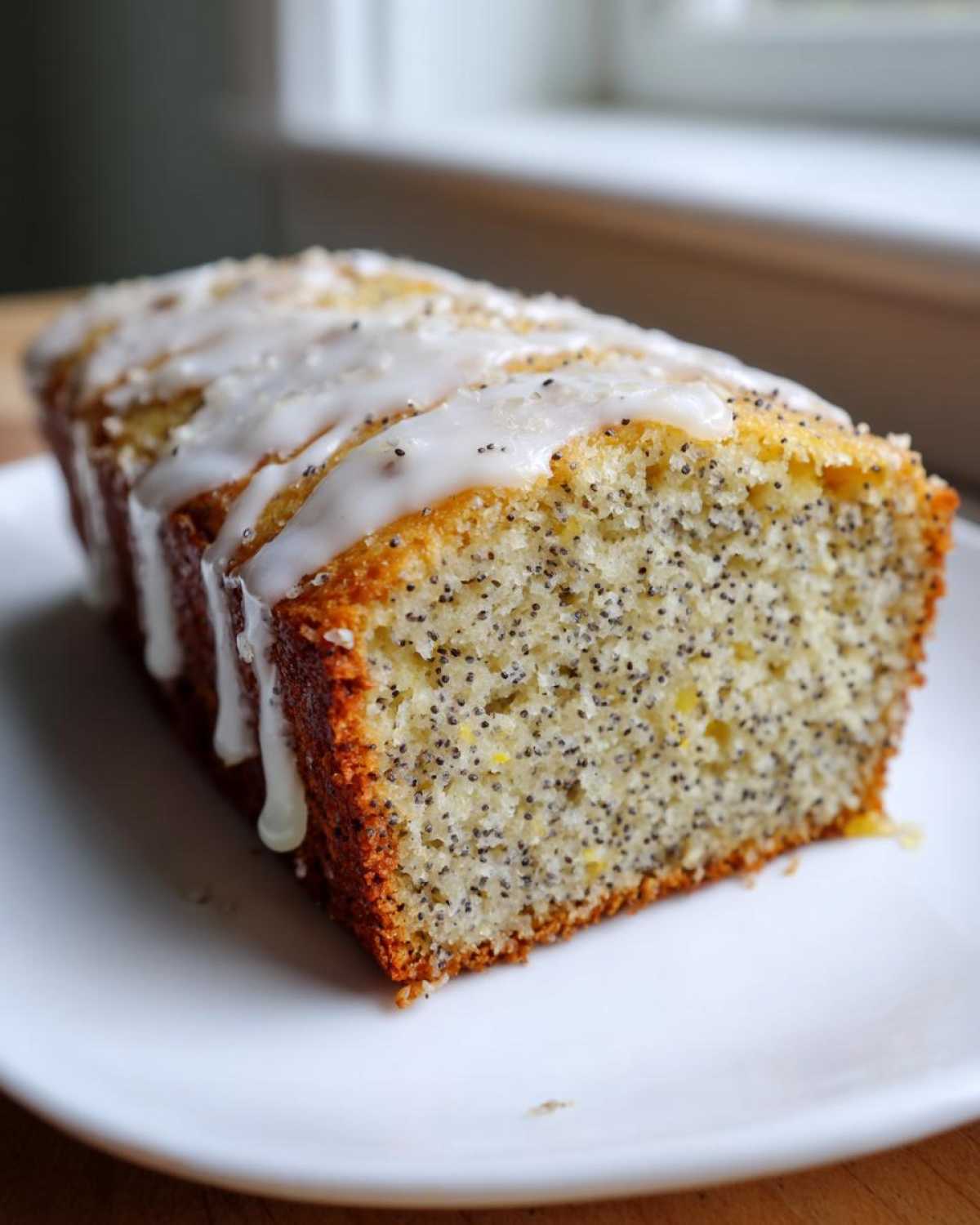 A close-up of a freshly baked Gluten-Free Lemon Almond Poppy Seed Cake loaf with white lemon glaze drizzled on top.