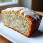 A close-up slice of moist Gluten-Free Lemon Almond Poppy Seed Cake topped with white glaze.