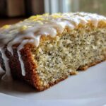 Close-up of a moist slice of Gluten-Free Lemon Almond Poppy Seed Cake with thick lemon glaze and zest.