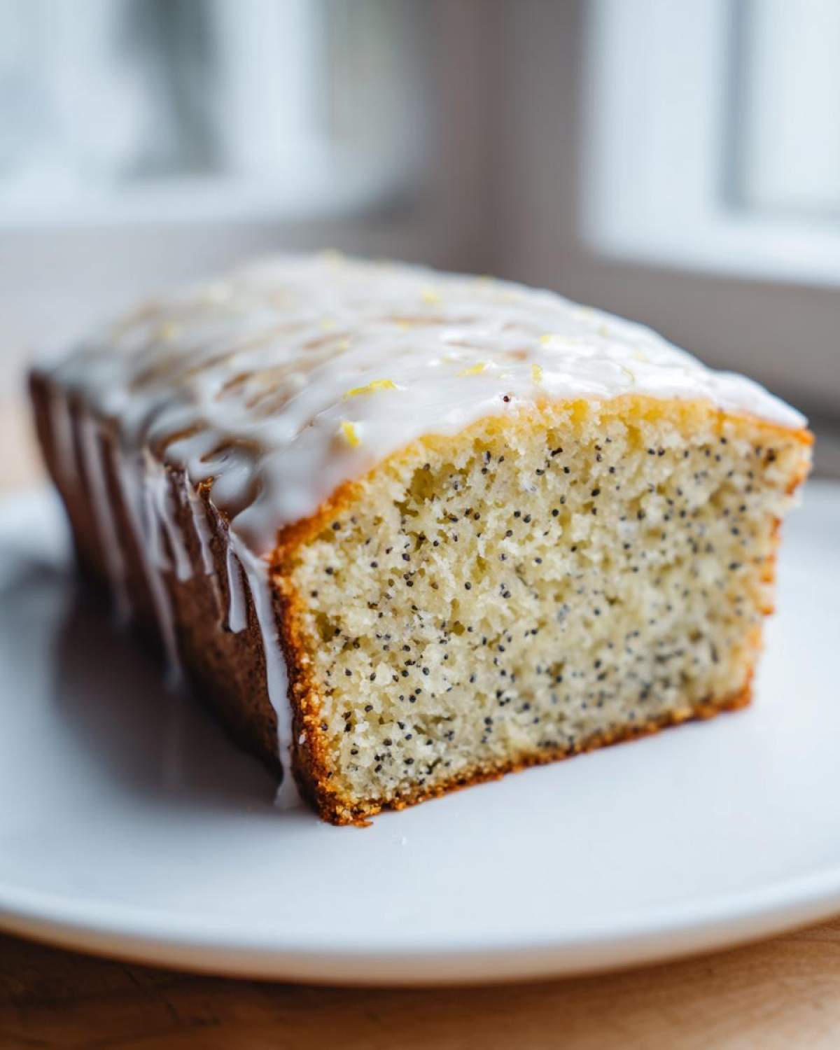 A close-up of a slice of Gluten-Free Lemon Almond Poppy Seed Cake with white glaze and lemon zest.
