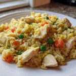 A close-up of a plate piled high with Gluten-Free Lemon Pepper Fried Rice featuring chicken pieces, carrots, peas, and scrambled egg.