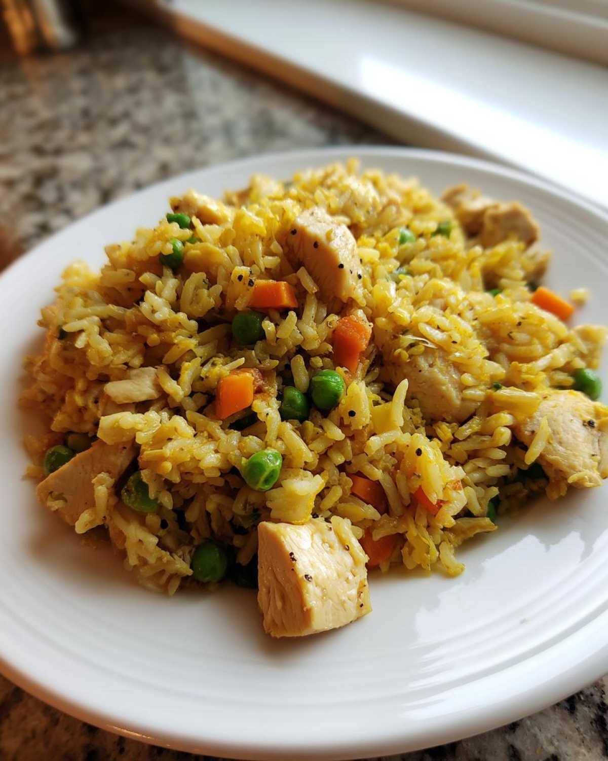 A close-up of Gluten-Free Lemon Pepper Fried Rice mixed with diced chicken, peas, and carrots on a white plate.