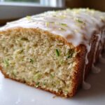 Close-up of a loaf of moist Gluten-Free Lemon Zucchini Bread topped with white glaze and lemon zest.