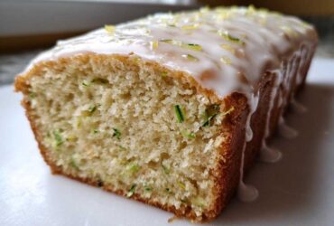 Close-up of a loaf of moist Gluten-Free Lemon Zucchini Bread topped with white glaze and lemon zest.