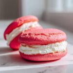 Close-up of two bright pink Gluten-Free Strawberry Lemon Whoopie Pies filled with thick white cream.