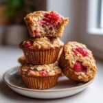 A stack of moist Gluten-Free Strawberry Oat Muffins topped with oats, with the top muffin broken open to show the berry interior.