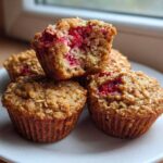 A stack of four Gluten-Free Strawberry Oat Muffins, one broken open showing the bright red fruit inside.