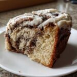 Close-up of a moist slice of cinnamon roll cake featuring swirls of cinnamon filling and thick white icing.