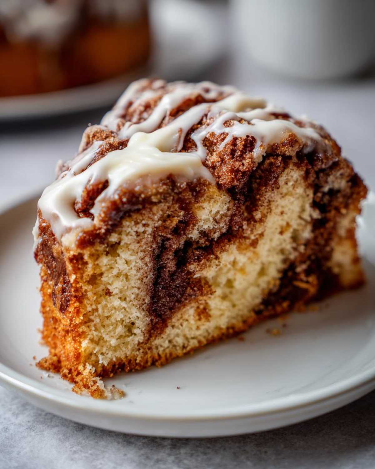 Close-up of a moist slice of cinnamon roll cake featuring swirls of cinnamon filling and drizzled with white vanilla icing.
