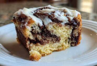 A close-up of a single, gooey slice of cinnamon roll cake topped with white icing.