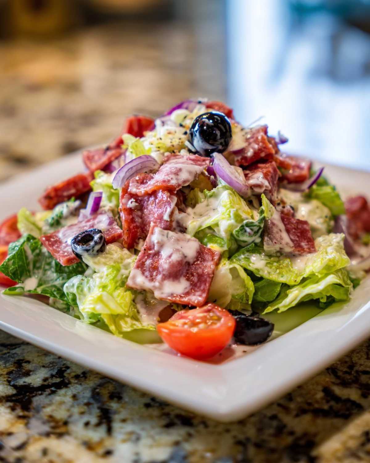A close-up of a vibrant grinder salad featuring lettuce, salami, red onion, tomatoes, olives, and creamy dressing.