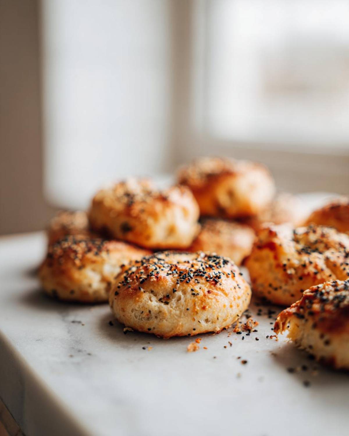 A close-up of golden baked High-Protein Cottage Cheese Bagel Bites topped with everything bagel seasoning on a white marble surface.