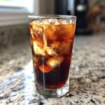 Close-up of Iced Brown Sugar Cinnamon Cold Brew with cream swirling into the dark coffee over ice cubes.