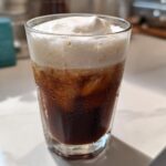 Close-up of a tall glass filled with Iced Coconut Mocha with Cold Foam topping.