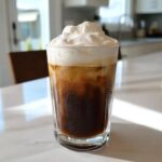 A tall glass filled with Iced Coconut Mocha with Cold Foam, showing condensation on the glass.