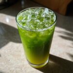 A tall glass filled with a vibrant green Iced Matcha Pineapple Refresher, topped with crushed ice.