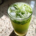 Close-up of a tall glass filled with an Iced Matcha Pineapple Refresher, topped with ice cubes and vibrant green foam.