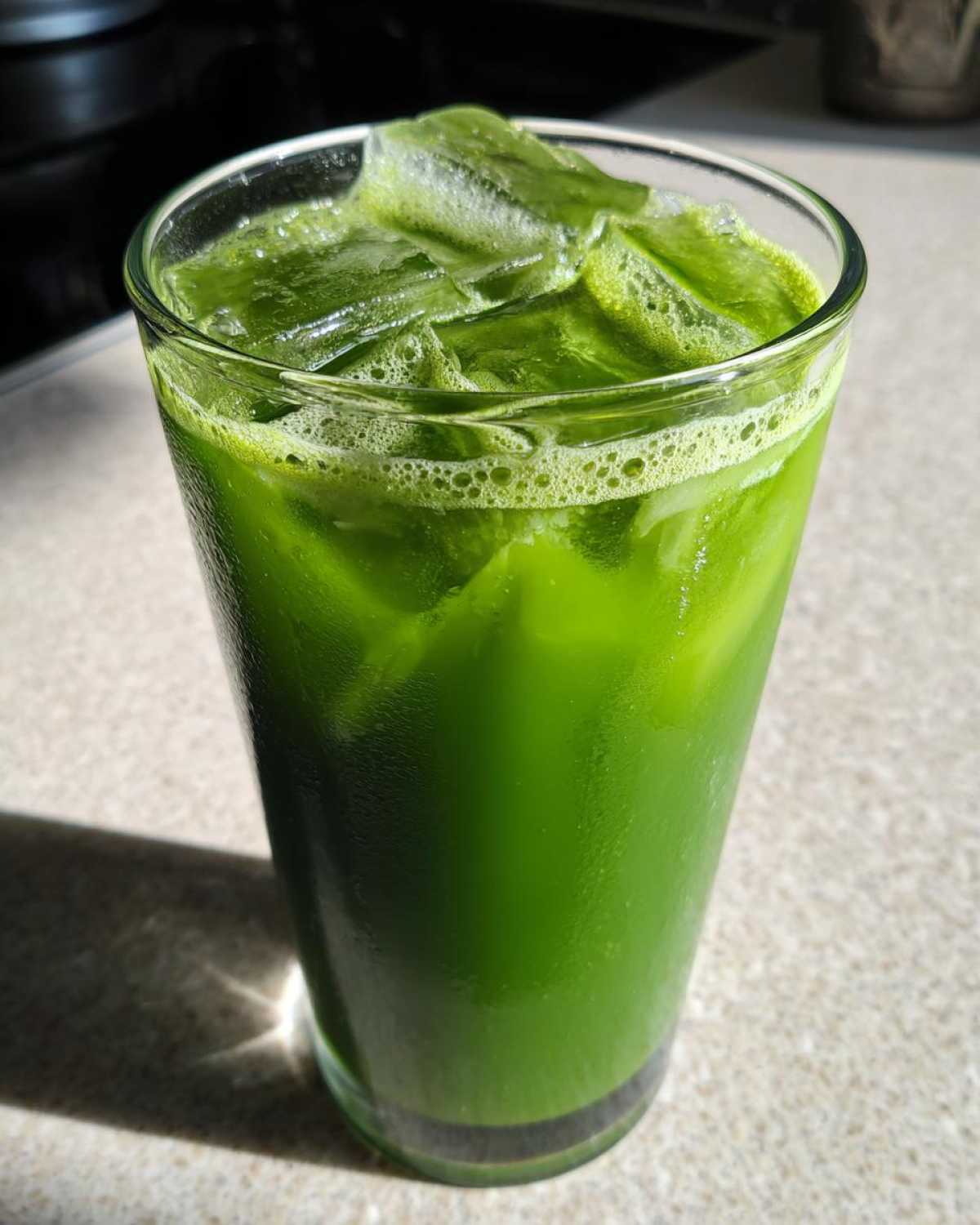 A tall glass filled with a vibrant green Iced Matcha Pineapple Refresher, packed with ice cubes and showing condensation.