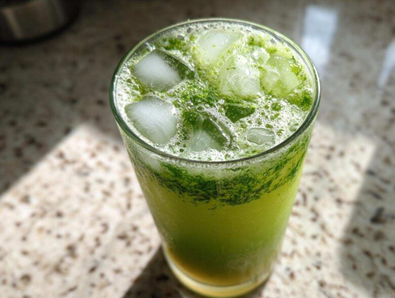 Close-up of a tall glass filled with an Iced Matcha Pineapple Refresher, topped with ice cubes and vibrant green foam.