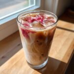 Close-up of a tall glass filled with Iced Raspberry Vanilla Chai, showing swirling milk, ice cubes, and raspberry syrup.