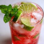 Close-up of a vibrant Iced Watermelon Lime Cooler filled with crushed ice, lime slices, and garnished with fresh mint.