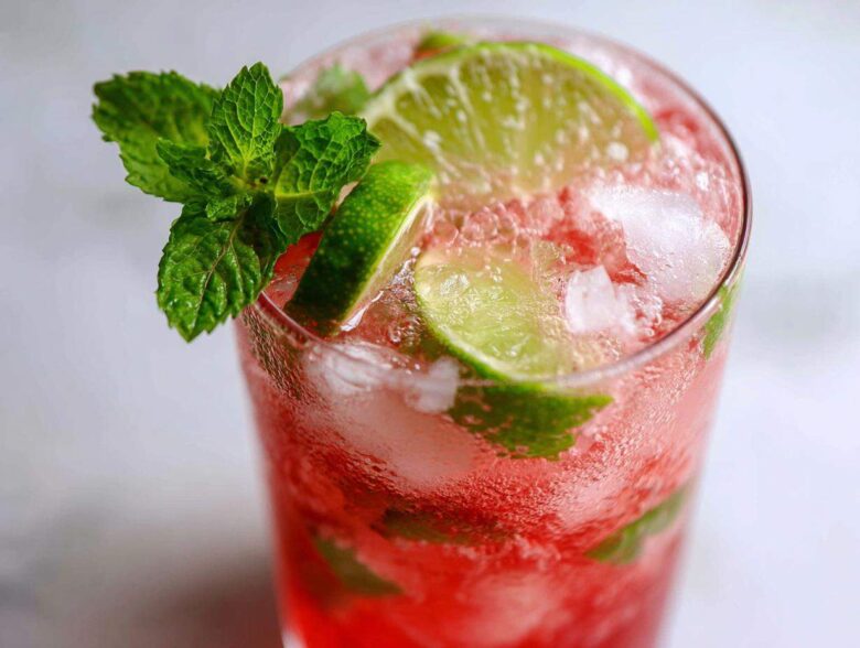 Close-up of a vibrant Iced Watermelon Lime Cooler filled with crushed ice, lime slices, and garnished with fresh mint.