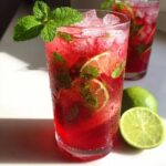 Close-up of a tall glass filled with a vibrant Iced Watermelon Lime Cooler, crushed ice, mint, and lime slices.